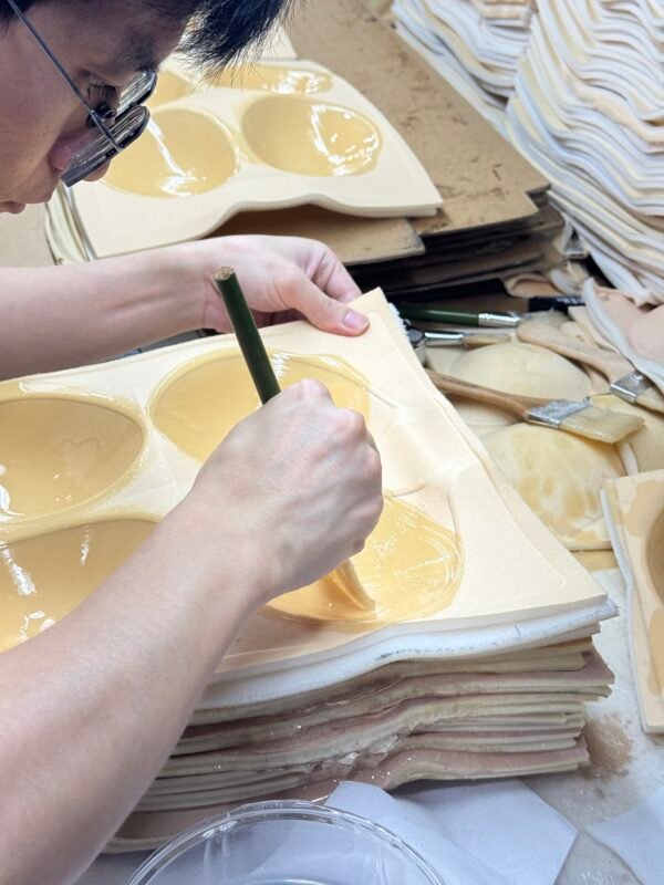 Manual brushing of silicone adhesive on adhesive bra cups.